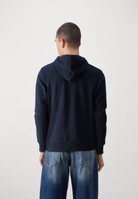 Sudadera con capucha azul marino con cordón en la capucha, puños acanalados y un ajuste relajado, combinada con jeans vaqueros azul claro desgastados.