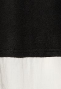 Section supérieure noire avec une finition texturée, passant à une section inférieure blanche lisse. L'ourlet est soigneusement cousu.