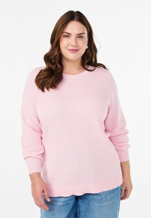 Suéter de textura rosa claro con cuello redondo, puños y dobladillo acanalados, combinado con jeans azul claro. Las novedades incluyen un patrón sutil.