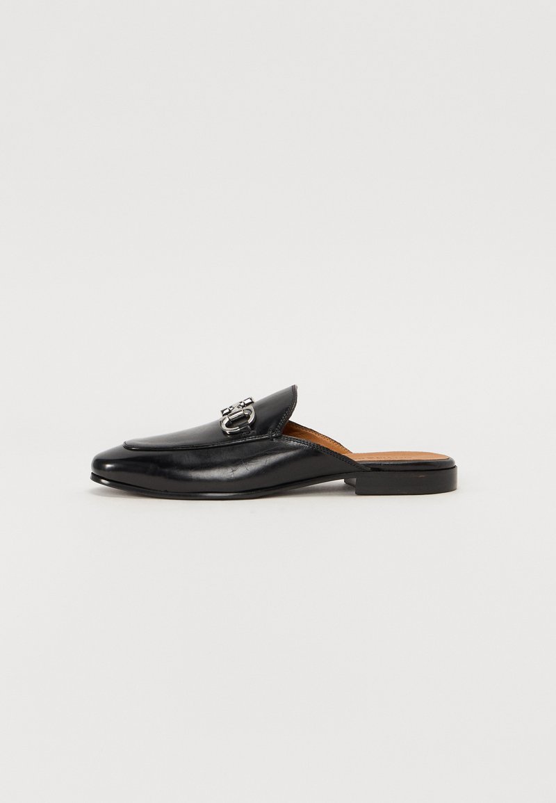 Melna ādas slip-on loafer ar nedaudz norādītu pirkstu, greznu sprādzi un zemu, kvadrātu papēdi. Gluda tekstūra un minimālistisks dizains.