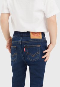 Mörkblå denimjeans med en gummibelagd Levi's-logotyp på baksidan av midjan, med klassiska sömmar och två bakfickor.