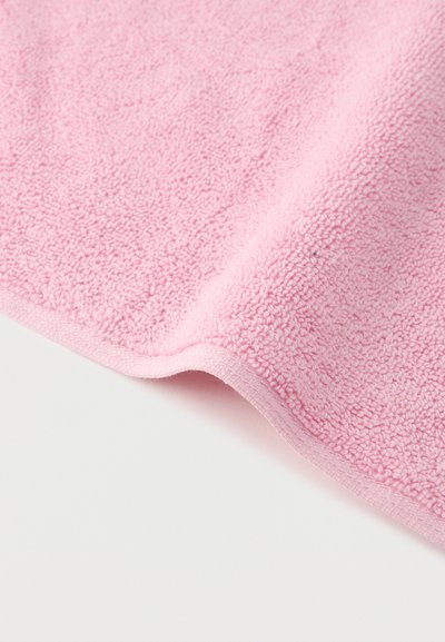 Μαλακό υφασμάτινο ύφασμα terry ροζ χρώματος με υφή βρόχων, διπλωμένο ελαφρώς πάνω σε λευκή επιφάνεια.