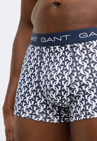 Marineblaue Boxer mit weißem geometrischem Muster, ausgestattet mit einem gebrandeten marineblauen elastischen Bund und einem figurbetonten Design. Weicher, elastischer Stoff.