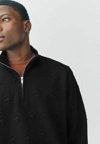 Sort lynlås sweatshirt lavet af tekstureret stof med et præget træmønster. Kraven står højt med en sølv lynlåsdetalje.