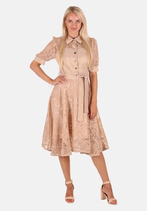 Beiges Kleid mit floralem Spitzenoverlay, kurzen Puffärmeln, Knopfleiste, Gürtel in der Taille und A-Linie Rock. Kombiniert mit nuden Blockabsatzsandalen.