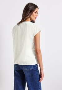 Blusa corta de manga corta en verde claro con un acabado texturizado, escote redondo y un corte holgado, combinada con jeans de mezclilla azul.