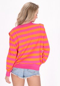Pulover supradimensionat în dungi vibrante de roz și portocaliu, cu manșete încrețite și decolteu rotund. Material moale tricotat, croială casual.