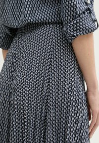 Marineblaues Kleid mit einem geometrischen Muster aus weißen und hellblauen Rechtecken. Faltendes Design aus einem weichen, strukturierten Stoff und umgeschlagenen Ärmeln.