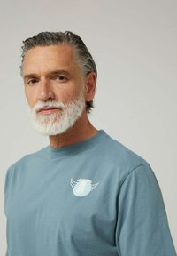 Camiseta de algodón azul claro con mangas cortas, con un pequeño gráfico en el lado izquierdo del pecho. Textura suave y diseño de cuello redondo.