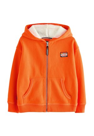 Felpa arancione con zip, foderata in morbido e peloso bianco, con tasche frontali e un logo a patch sul lato sinistro del petto. Maniche lunghe e polsini a costine.