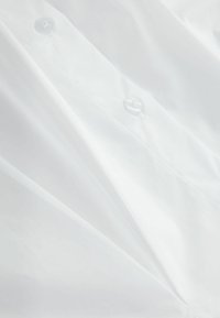 White button-up shirt with a smooth texture, featuring clear plastic buttons and crisp fabric that showcases clean lines and tailored design.