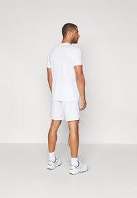 T-shirt sportivo bianco e pantaloncini, realizzati in tessuto leggero. Presenta maniche corte e una vestibilità slim, abbinati a scarpe da ginnastica.