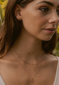 Rosenvergoldete, geschichtete Halsketten an einem Modell, mit einer zarten Kette und einem runden Anhänger; glatte Textur und minimalistisches Design.