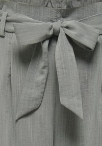 Ceinture en tissu gris nouée en un nœud autour d'un pantalon taille haute avec un détail subtil de texture verticale.