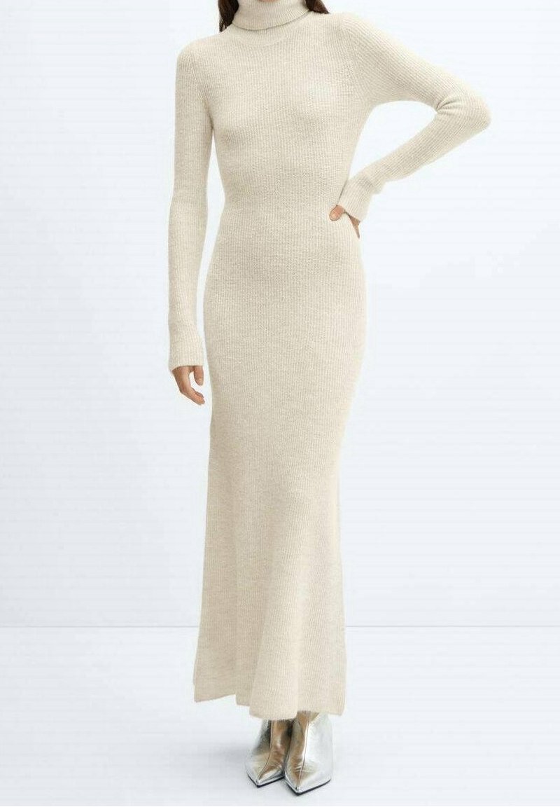 Robe à col roulé beige en texture côtelée, coupe ajustée, manches longues, et ourlet jusqu'au sol ; portée avec des escarpins pointus argentés.