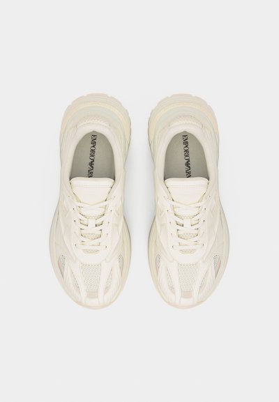 Paire de baskets à lacets Emporio Armani de couleur blanc cassé avec détails en mesh et cuir, vues de dessus sur un fond uni.