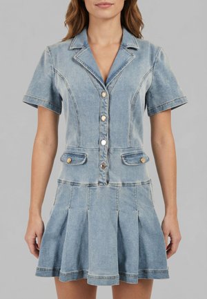 Vrouw draagt een lichtblauw denim jurk met korte mouwen, knopen, een uitgesneden kraag, klepzakken en een geplooide rok.