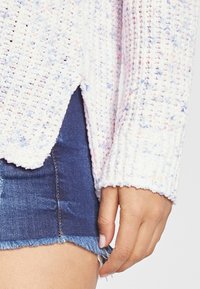 Gestreifter Pullover in Pastellfarben mit strukturiertem, geschlungenem Garn. Verfügt über einen seitlichen Schlitz und gerippte Bündchen. Kombiniert mit einem Jeans-Minirock.