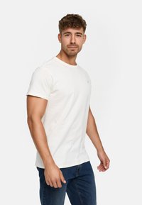 Weißes Baumwoll-T-Shirt mit Rundhalsausschnitt und kurzen Ärmeln, mit einem kleinen Logodetail auf der Brust, kombiniert mit blauen Denim-Jeans.