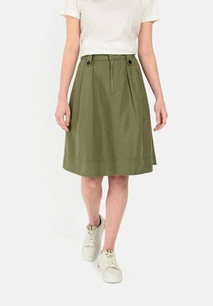 Jupe plissée vert olive avec une texture lisse, présentant deux boutons à la taille, associée à des baskets blanches.