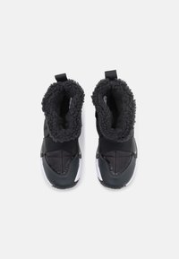 Svarta stövelliknande skor med mjukt, pälsaktigt foder och kviltad yta. Har en hållbar utsida och en kontrasterande vit sula.