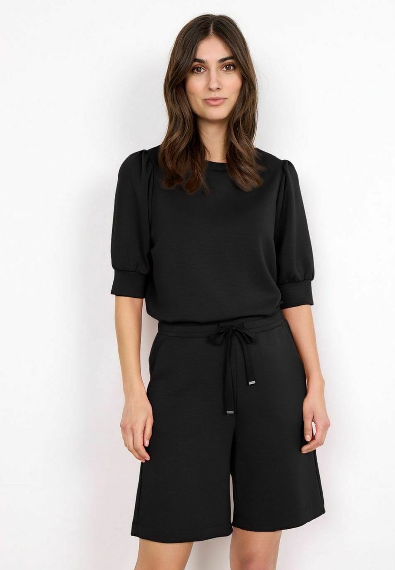 Černý dvoudílný outfit složený z trička s krátkým rukávem a kulatým výstřihem a šortek s nastavovací šňůrkou, které mají uvolněný střih a hladkou texturu.