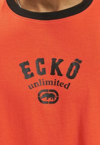 Top din bumbac portocalie, cu bretele, având un decolteu negru și un print grafic cu textul "ECKŌ unlimited" și un rinocer stilizat.