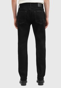Jeans negros de corte ajustado, con una textura suave, dos bolsillos traseros con bordes angulados y un discreto parche con el logo en la cintura.