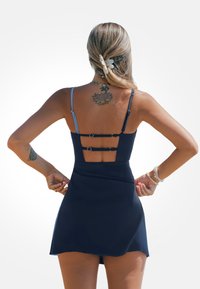 Granatowa sukienka kąpielowa z regulowanymi cienkimi ramiączkami, otwartym tyłem z metalowymi akcentami oraz rozkloszowanym dołem.