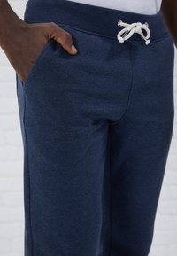 Pantalons de survêtement bleu marine en tissu doux avec une taille élastique, fermeture à cordon et poches latérales. Texture lisse avec des détails minimes.