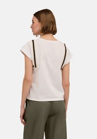 Tricou alb cu mâneci scurte, având dungi negre și ivoriu pe umeri. Material din bumbac moale, croială lejeră.