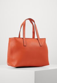 Pomarańczowa torba typu tote o teksturowanej powierzchni, z dwoma krótkimi uchwytami, prostokątnym kształcie i kontrastującym, szarym przeszyciem wzdłuż krawędzi.