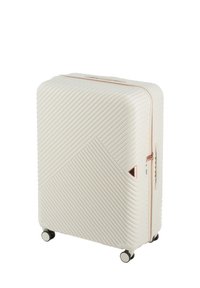 Valise rigide de couleur crème avec une texture à nervures diagonales. Équipée de matériel en or rose, d'une fermeture éclair et de quatre roulettes pivotantes.