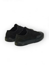 Baskets en daim noir au design bas profil, avec un bout cap en texture et une semelle en caoutchouc lisse. Elles possèdent des lacets plats et un logo discret sur le talon.