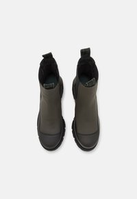 Waterproof ankle boots in dark green and black, featuring a smooth rubber-like upper, textured accents, and sturdy lug soles for traction.