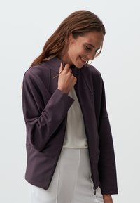 Giacca viola con zip e colletto alto, dal taglio rilassato. Realizzata in un tessuto liscio, con dettagli a coste e maniche lunghe.