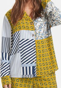 Multicolore overhemd met knopen, featuring een mix van vierkanten, strepen en bloemmotieven in geel, blauw en wit met lange mouwen.