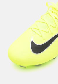 Felle gele voetbalschoen met een gestructureerde synthetische bovenkant, zwarte Nike-swoosh en vetersluiting. Beschikt over ronde noppen voor grip.