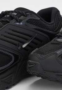 Gros plan de deux chaussures de sport noires en mesh et matériaux synthétiques, avec des boucles de lacets réfléchissantes et un logo Nike swoosh noir.