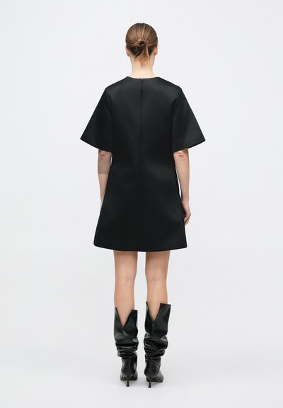 Sort kortærmet kjole med enkel, lige silhuet og lynlås bagpå. Kombineret med knæhøje, sorte, løstsiddende støvler.