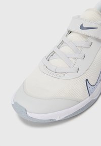 Biała sportowa buty z siateczkową cholewką, szarymi akcentami, zawiązywaniem na sznurówki i rzep, okrągły czubek oraz teksturowana podeszwa o minimalistycznym designie.