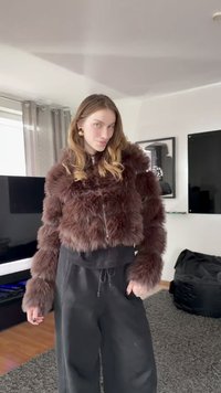 Brązowa kurtka o krótkim kroju z grubym, puszystym futerkiem i zamkiem błyskawicznym. Noszona do czarnych, wysokich spodni, z długimi rękawami i okrągłym dekoltem.