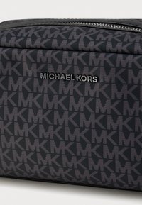 Μαύρη τσάντα από νάιλον με επαναλαμβανόμενο μοτίβο «MK». Διαθέτει εμφανές ασημένιο λογότυπο «Michael Kors» και φερμουάρ. Υφή επιφάνειας.