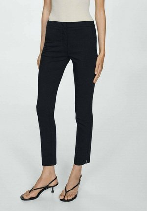 Schwarz geschnittene, knöchellange Hose in Slim-Fit, kombiniert mit schwarzen, Riemchen-Heels und einem beigen ärmellosen Oberteil.