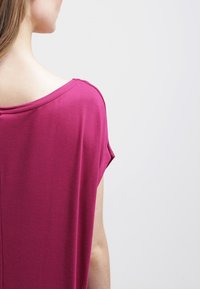 Magenta short-sleeve top with a scooped neckline, soft texture, and relaxed fit, featuring stitching details along the shoulder seams.