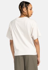Luźna koszulka z krótkim rękawem w odcieniu off-white, wykonana z bawełny. Posiada okrągły dekolt oraz nieco dłuższy tylny brzeg.