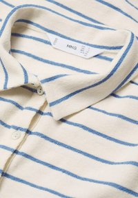 Polo a righe in morbido tessuto crema, con righe orizzontali azzurro chiaro, colletto e patta con due bottoni. Etichetta del marchio visibile.