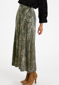 Maxisukně z průsvitné látky se zeleným a béžovým leopardím potiskem, s plisovaným designem, doplněná o světle hnědé špičaté kotníkové boty.