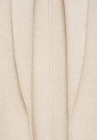 Gros plan sur un tissu tricoté beige avec une couture verticale visible et des bords repliés.