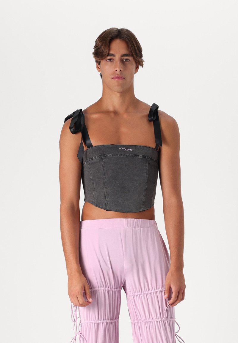 Top corto de mezclilla negra con tiras de cinta, que presenta un diseño estructurado y un dobladillo curvado. La modelo lleva pantalones recogidos en rosa claro.